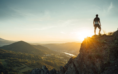  Silhouette of the person on the high rock at sunset. Satisfy hiker enjoy view. Tall man on rocky...
