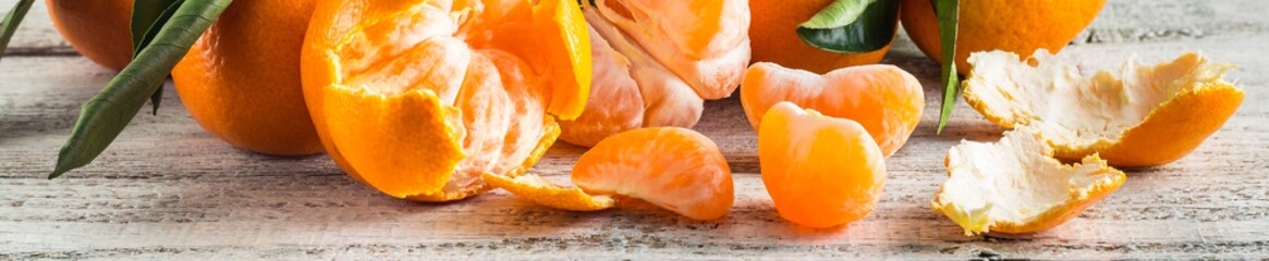 Banner of orange tangerines with green leaves on white wooden background. Peeled mandarin slices