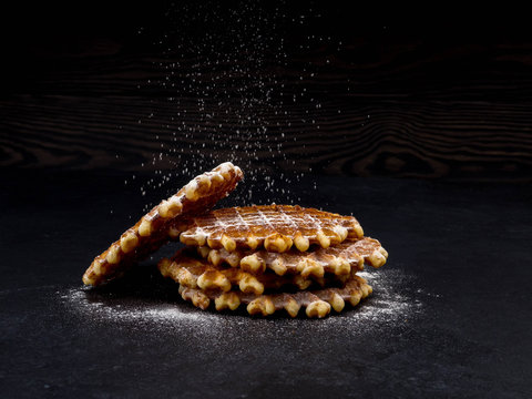 White plate with homemade Belgian waffles, on top of poured sifting of powdered sugar on black background, very tasty snack. sugar over old wooden table. 