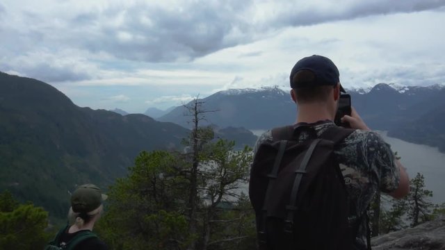 white young male using cell phone to record mountains after accomplishing hike in BC, smarting phone taking video of nature 60fps, 120 fps slowed down super slow.