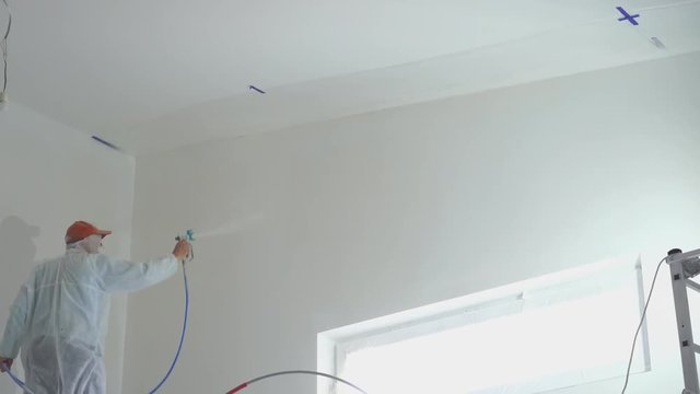 repair of the apartment - professional painter paints the walls with white paint spray gun