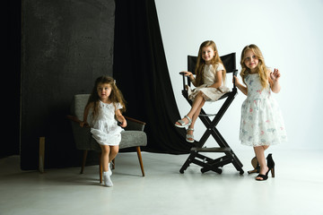 Interaction of children with adult world. Cute girls wearing mum's oversize shoes and dress for being older like she is. Little female models trying on clothes at home. Childhood, style, dream concept