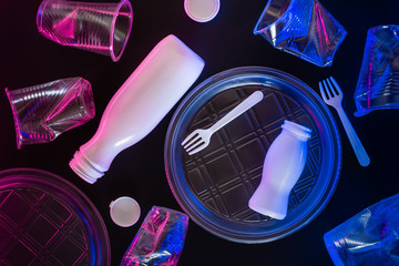 Plastic transparent tableware in neon lighting on black background. Environmental pollution concept