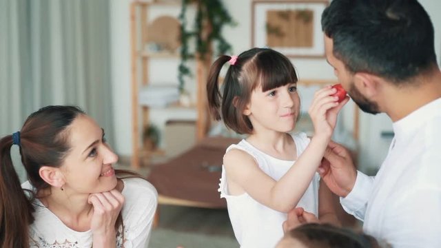 Happy family in kitchen, mom, dad and daughters eat strawberries, slow motion