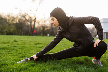 Portrait of muslim serious woman dressed in religious black hijab stretching her body while doing...