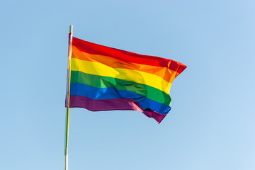 The bright rainbow gay flag is waving on the wind against blue sky background