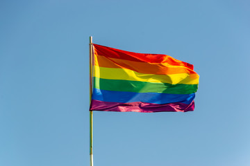 The bright rainbow gay flag is waving on the wind against blue sky background