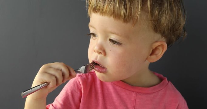 Baby with fork in mouth on gray background