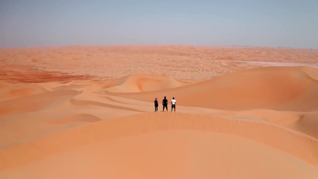 Cinematic drone shot of three friends standing on a top of sand dune in a desert