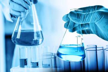 hand of scientist holding flask with lab glassware and test tubes in chemical laboratory background, science laboratory research and development concept