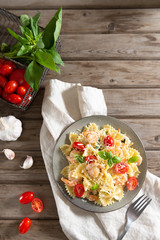 Pasta farfalle with shrimps, garlic sauce, cherry tomatoes and basil leaf on wooden table, italian cuisine, top view. Close up, copy space