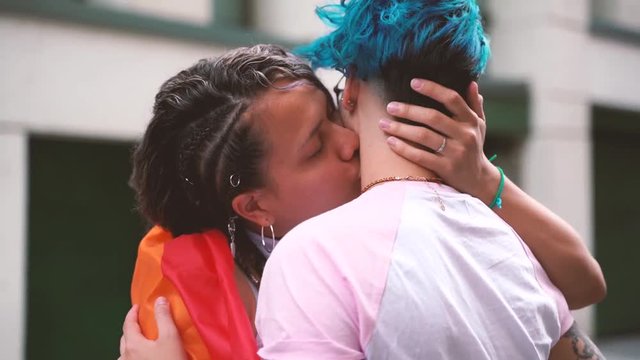 lesbian couple wearing with pride a lgbt flag and kissing on the street. Love is love. Freedom of showing affection between same gender couple.
