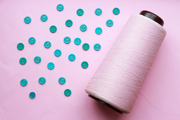 Bobbin with thread and blue buttons on a pink background close-up, concept of accessories for sewing.