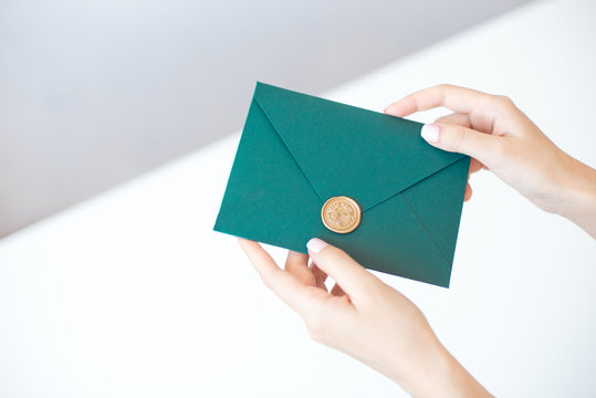 Close-up photo of female hands holding a green invitation envelope with a wax seal, a gift certificate, a postcard, a wedding invitation card