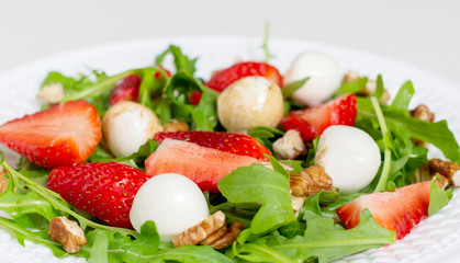 Salad with mozzarella cheese, arugula and strawberries on a white plate. Healthy summer green salad for diet, snack or light dinner.