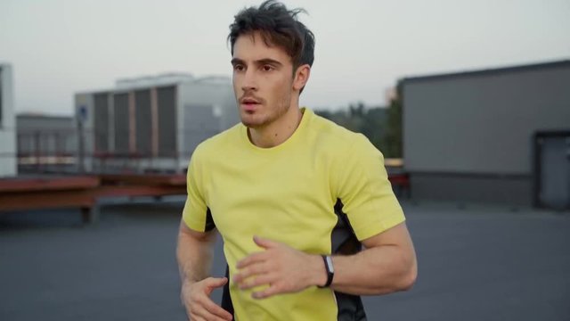 handsome sportsman in yellow sportswear running on rooftop