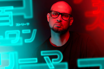 Attractive bald man with beard in glasses on neon light background