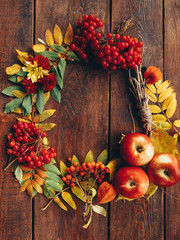 Autumn wrench decor. Colorful fall plants, leaves arranged in round frame on brown wooden background. Copy space.