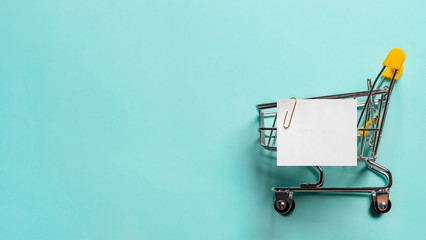 Shopping cart and white paper note list over blue background. Shopping concept on blue background....