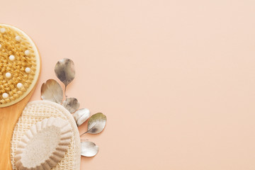 Spa therapy essentials. Cropped top view of wooden body brush, organic loofah and handmade soap. Peach background. Copy space.