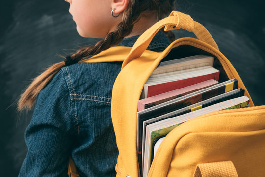 Back to school. Back view of young girl ready to study, with open backpack full with books.