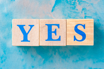 Wooden cubes with word YES on blue table.