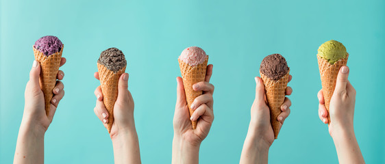 Hands holding ice cream in cones on blue background. Ice cream scoop in cones assortment in woman...