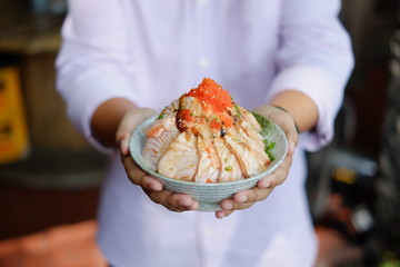 Hand hold Bowl of Rice with Salmon aburi (grilled) and Ikura (Roe) Don on blur background