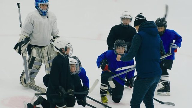 Boys in hockey sportswear skating closer to trainer on ice arena, who drawing scheme of positioning of players on marker board