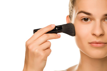 Portrait of young woman applying powder foundation with brush on white background
