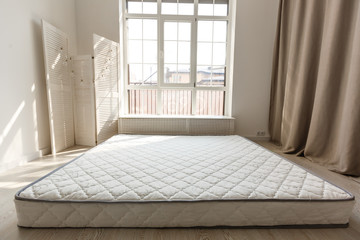 Grey mattress on the floor against designer screen in spacious bedroom with grey chair against dark curtain