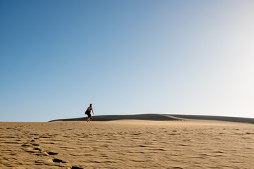 young confident woman walking alone on desert sand among dunes on a hot sunny day with clear blue sky
