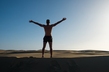 Fototapeta na wymiar young man standing on top of sand desert dune with open arms as a symbol of being young and free and wanderlust