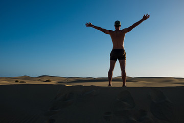 Fototapeta na wymiar young man standing on top of sand desert dune with open arms as a symbol of being young and free and wanderlust