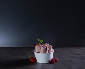 Delicious rolled Thai pink ice cream on dark table with dark background and berries