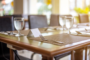 The tables and chairs in the restaurant with full set preparation next to the window with flare in the afternoon. 