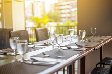 The tables and chairs in the restaurant with full set preparation next to the window with flare in the afternoon. 