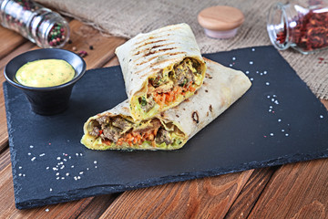 Close up view on Shawarma sandwich, gyro fresh roll in lavash. Shaurma served on black stone. Kebab in pita with copy space. Traditional Middle Eastern snack, fast food. Horizontal close up