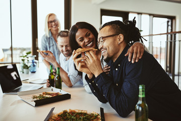 Office colleagues laughing over pizza and beers after work
