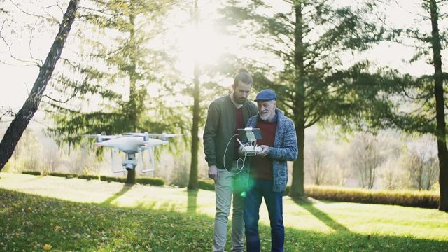 Senior father and his son with drone in nature, talking.