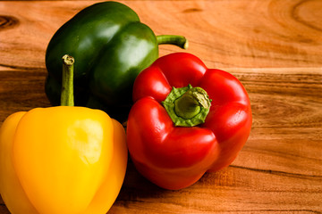 Fresh red, green and yellow capsicum on a wooden board, close up.