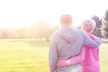 Rear view of senior couple in sportswear standing arms around in park