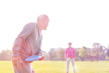 Senior man throwing flying disc towards woman in park