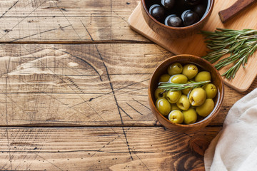 Black and green olives in wooden bowls on wooden table. Top view with space for text.