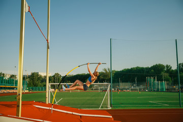Professional female pole vaulter training at the stadium in sunny day. Fit female model practicing...