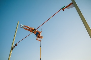 Professional female pole vaulter training at the stadium in sunny day. Fit female model practicing...