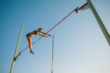Professional female pole vaulter training at the stadium in sunny day. Fit female model practicing in high jumps outdoors. Concept of sport, activity, healthy lifestyle, action, movement, motion.