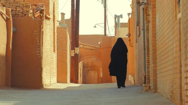 Muslim woman in traditional chador walking on street in Old city of Yazd, Iran
