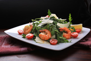 Salad with arugula and cherry tomatoes with shrimp, slices of lomon and parmesan.