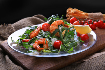 Salad with arugula and cherry tomatoes with shrimp, slices of lomon and parmesan.